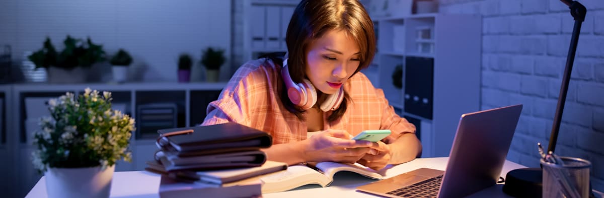 Potential student sitting at desk at home reading phone