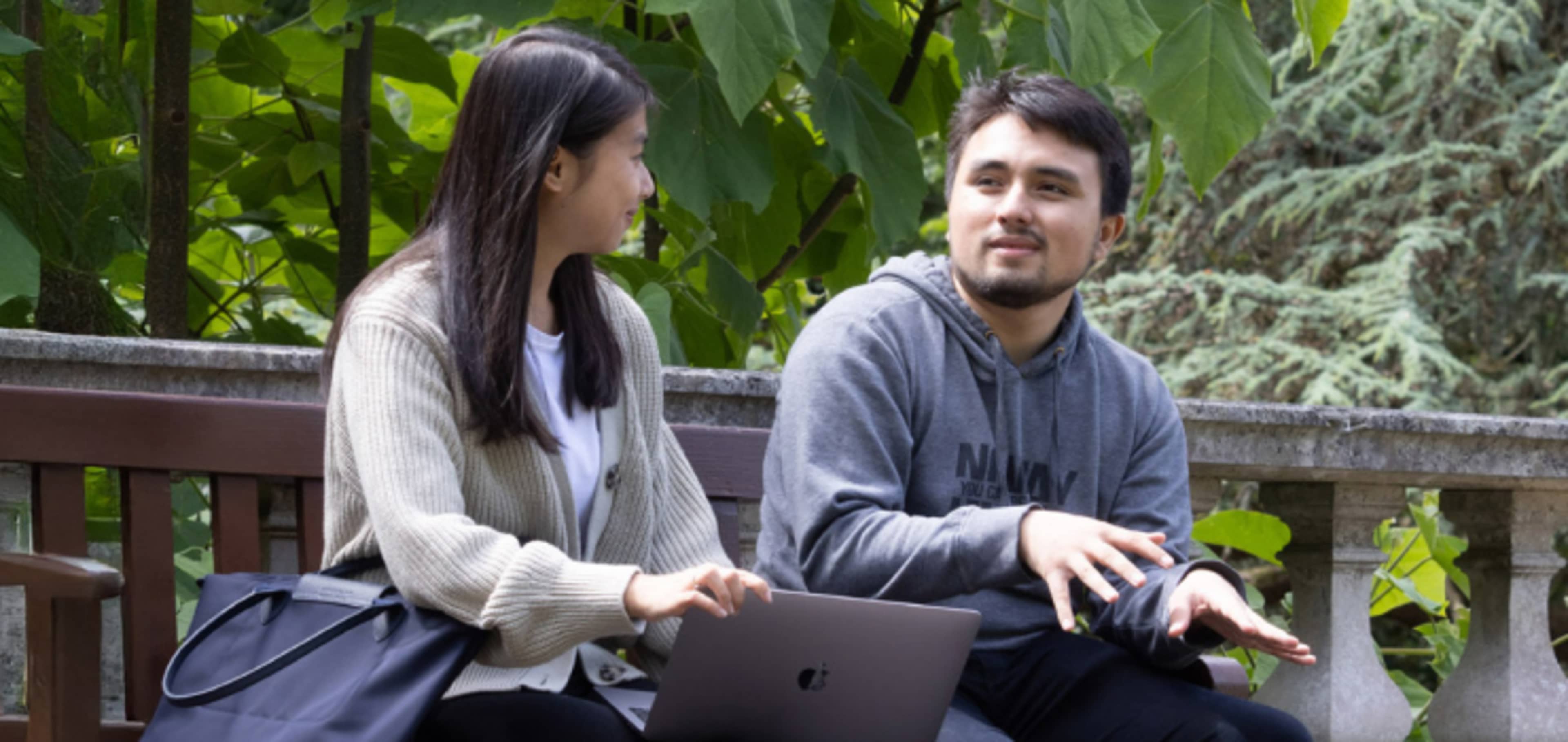 Two English language students working together at a desk with classmates in background