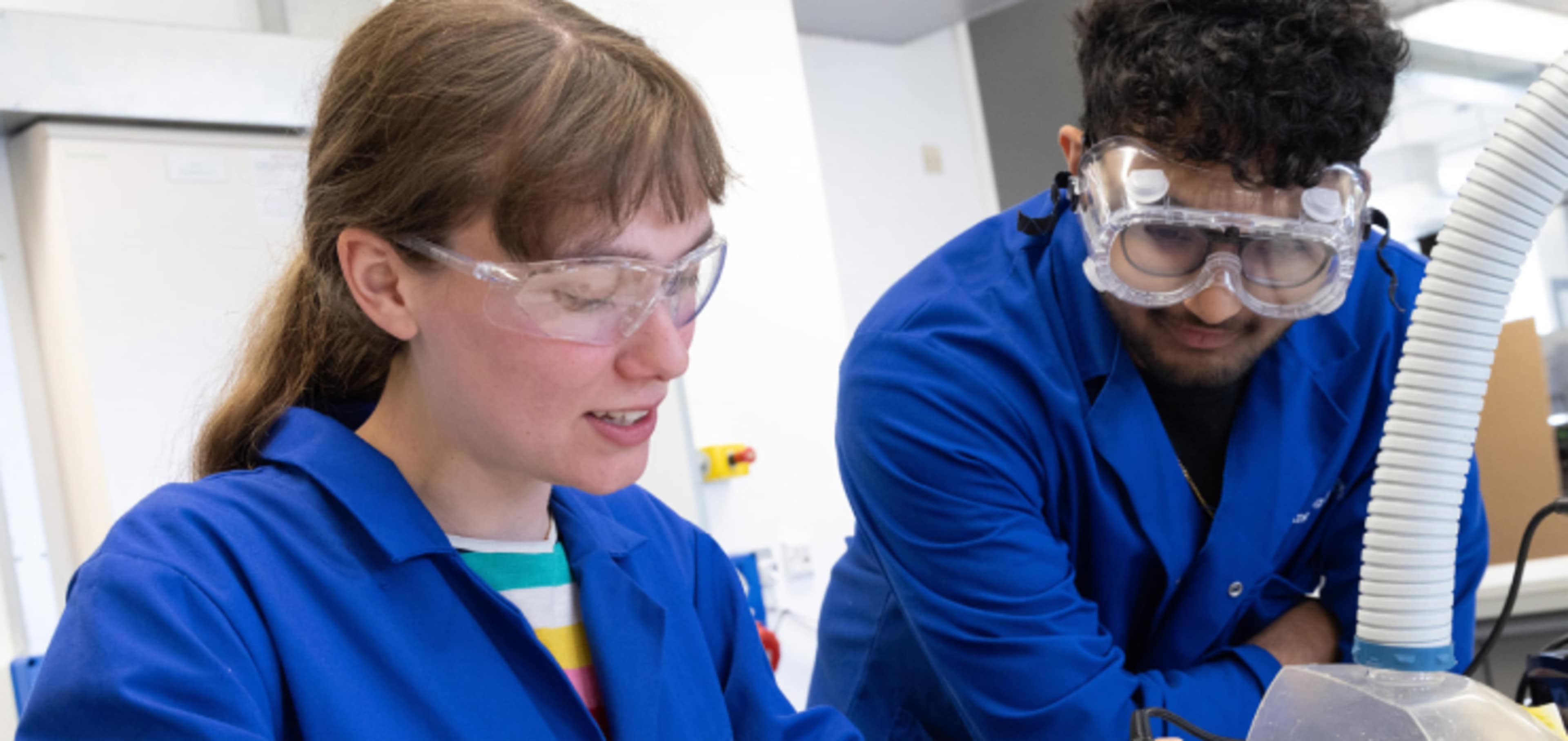 Two undergraduate engineering students working on project in lab wearing personal protective equipment 