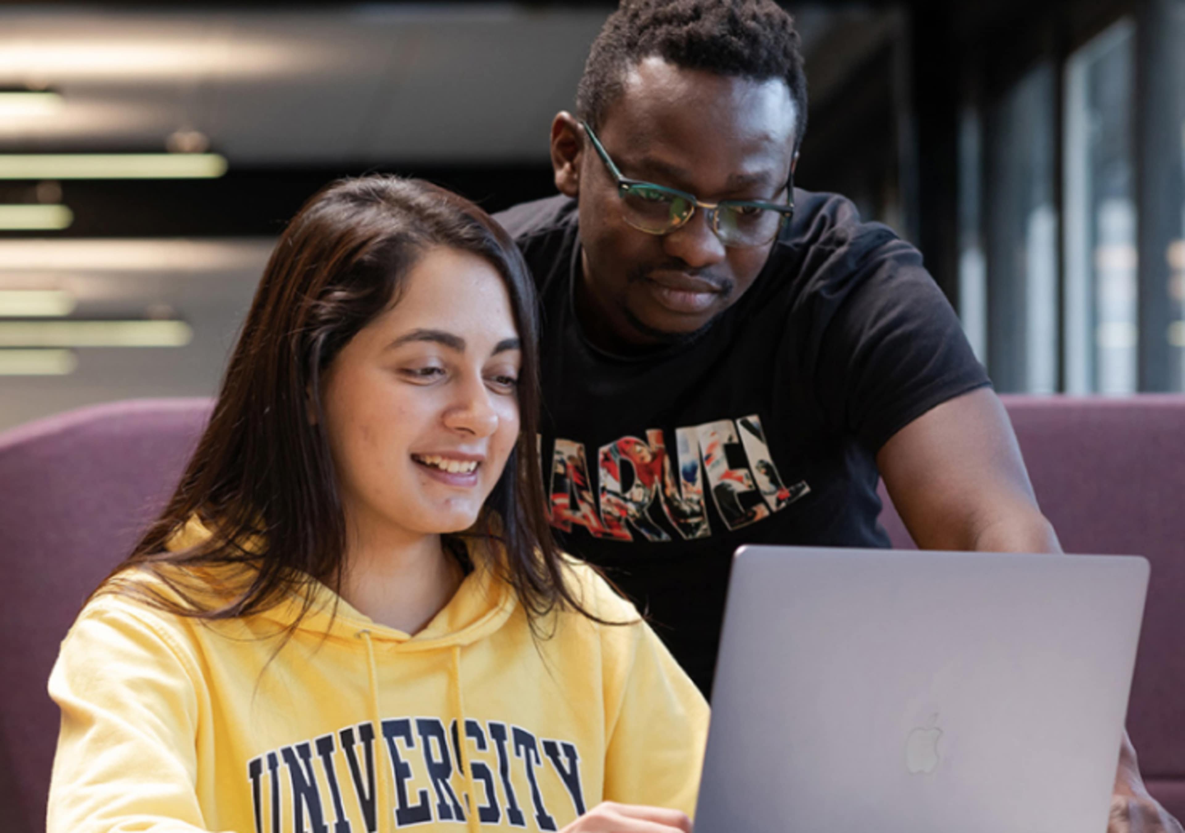 Young woman using her laptop and being assisted by a man