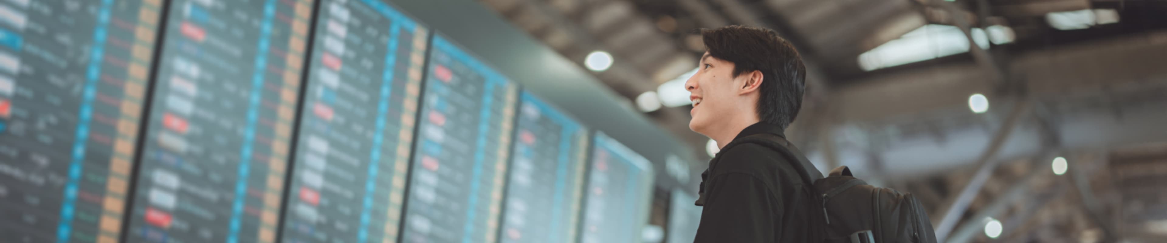 International student smiling while looking at the arrival board in the airport 