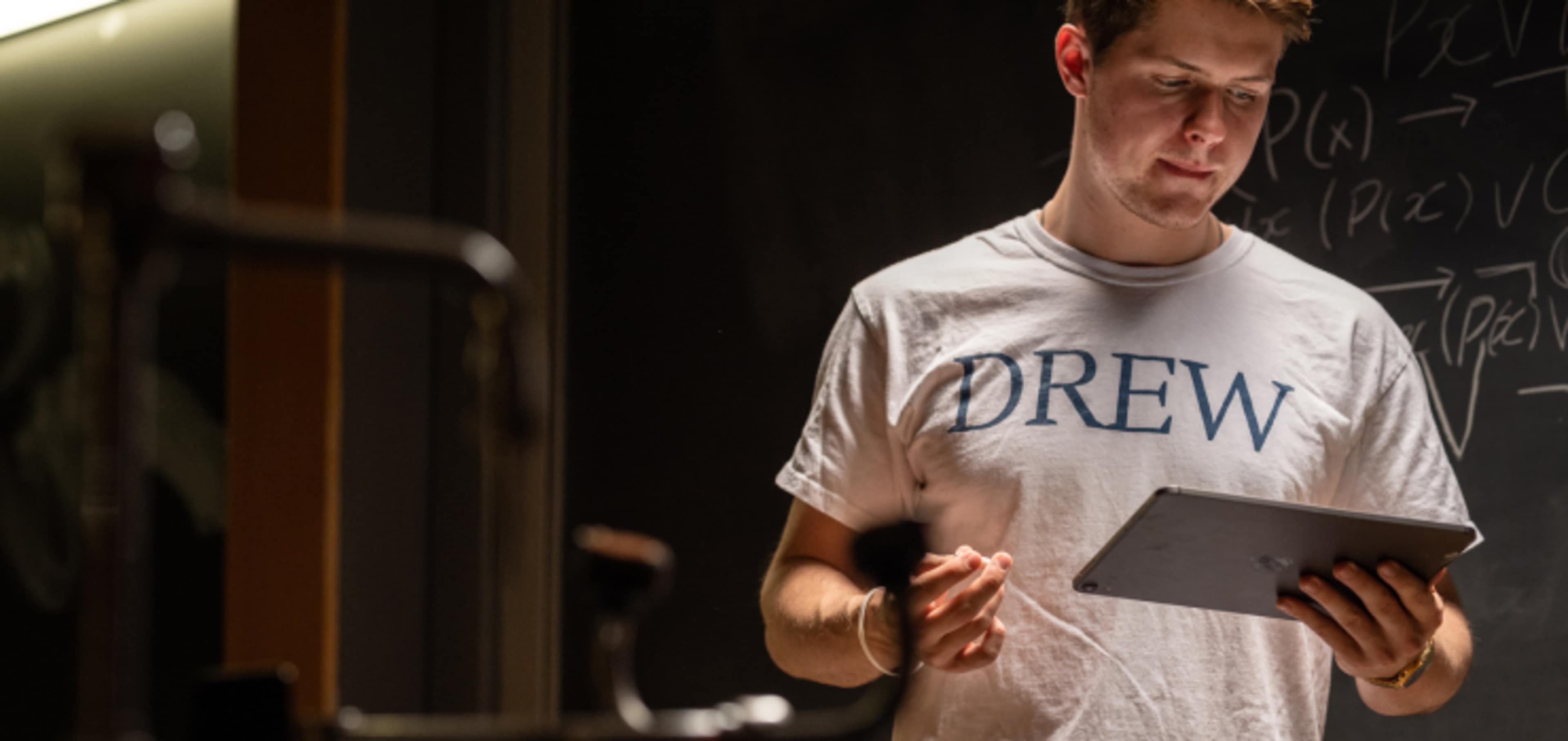 Cybersecurity student looking at tablet with equations on chalkboard 