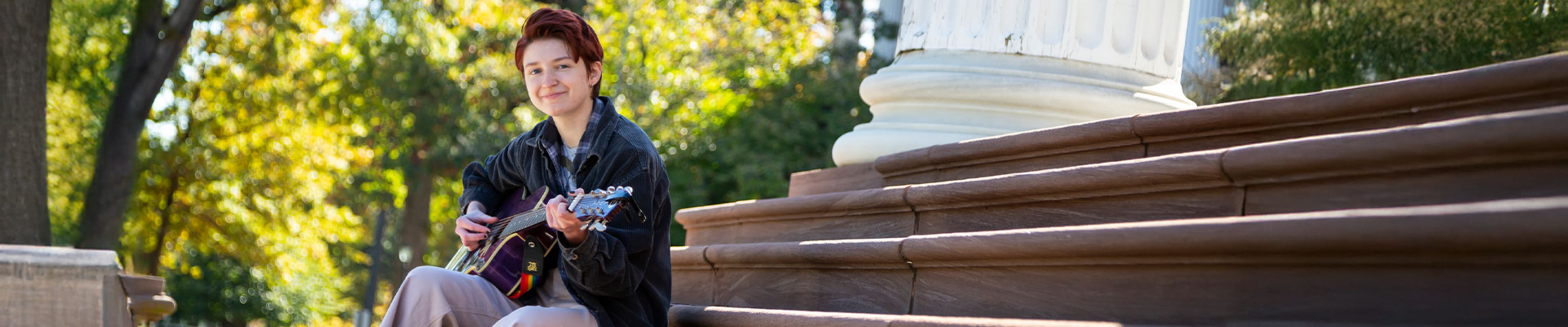 Student playing the guitar while sitting in the stairs